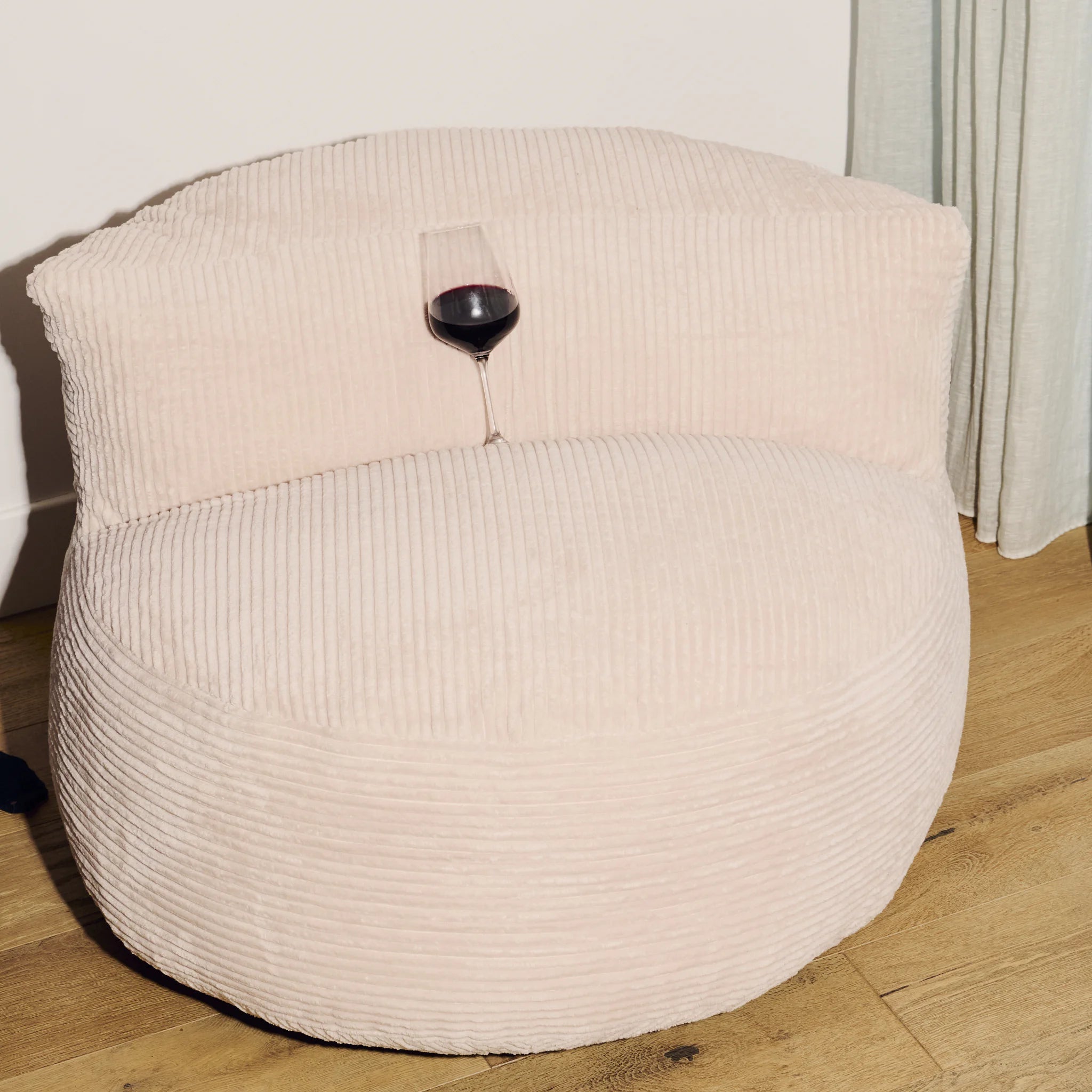 Beige bean bag chair with a glass of red wine on a wooden floor.