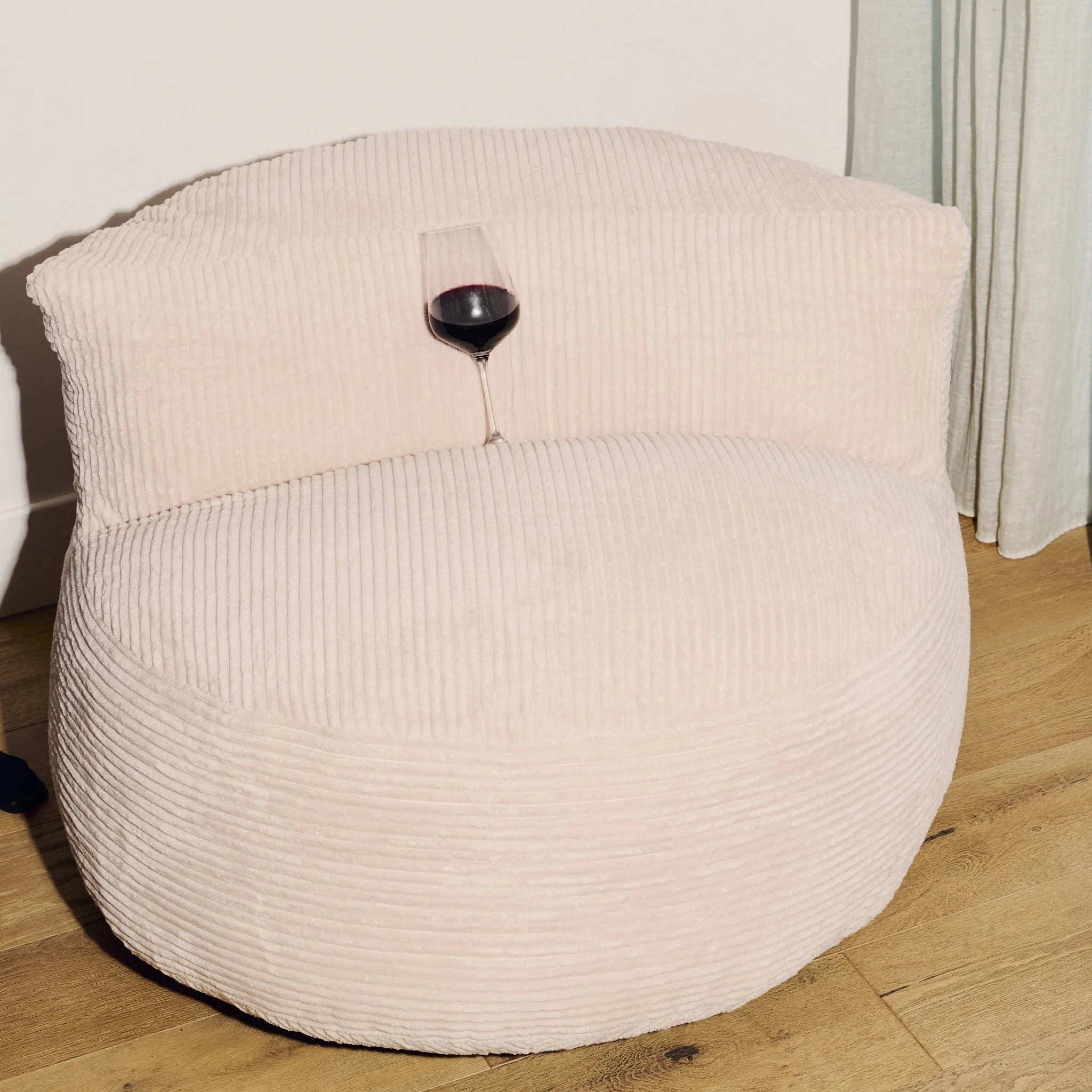 Beige bean bag chair with a glass of red wine on a wooden floor.
