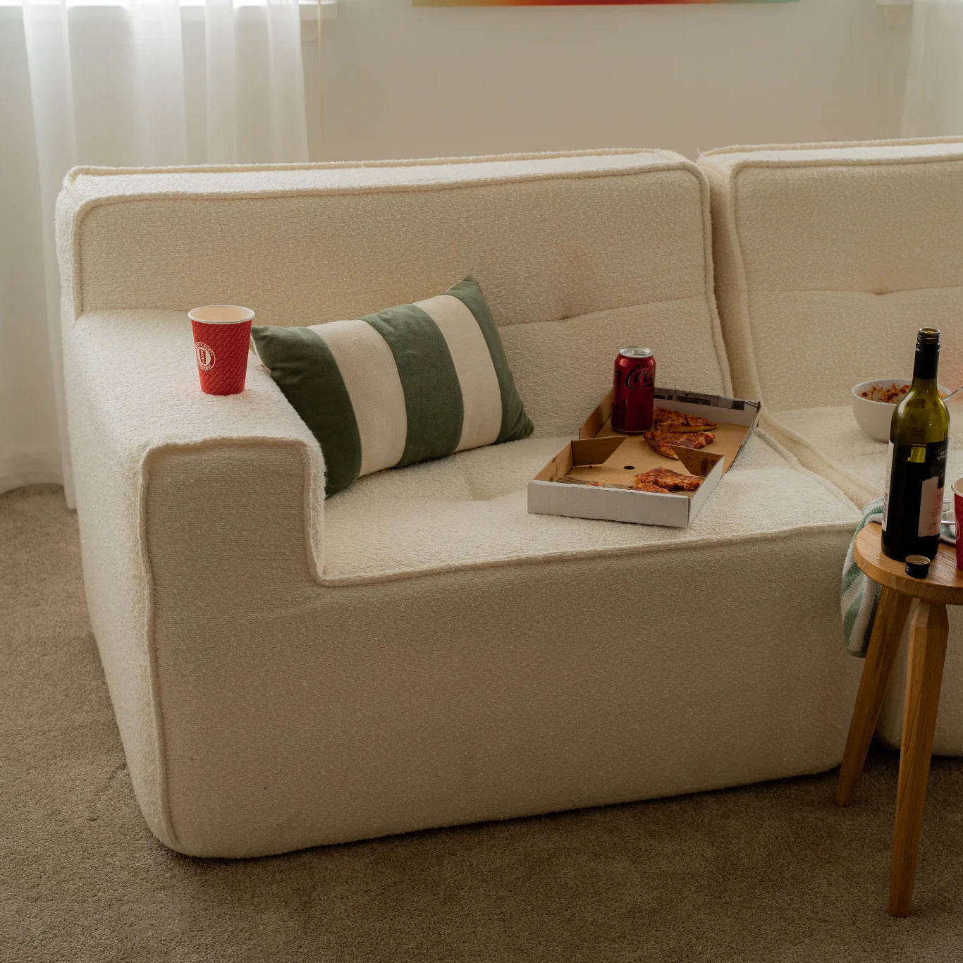 Beige sofa with a pizza box, red cup, and bottle of wine on a small table in a living room.