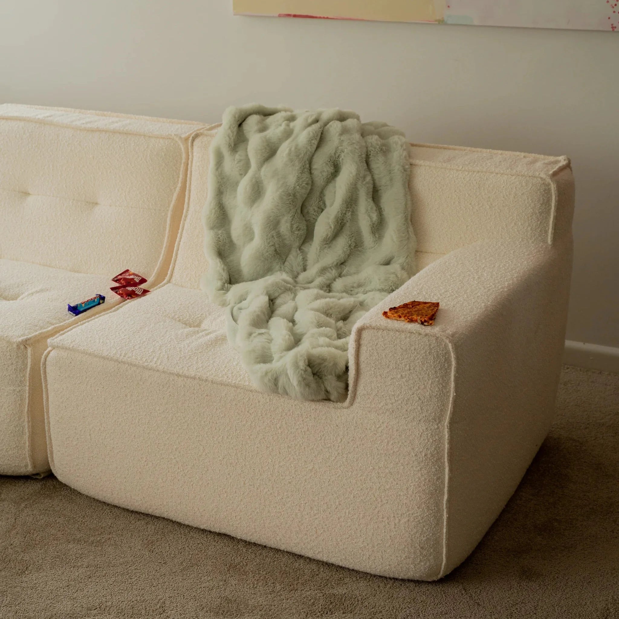 Beige sofa with a green textured blanket draped over it in a room setting.