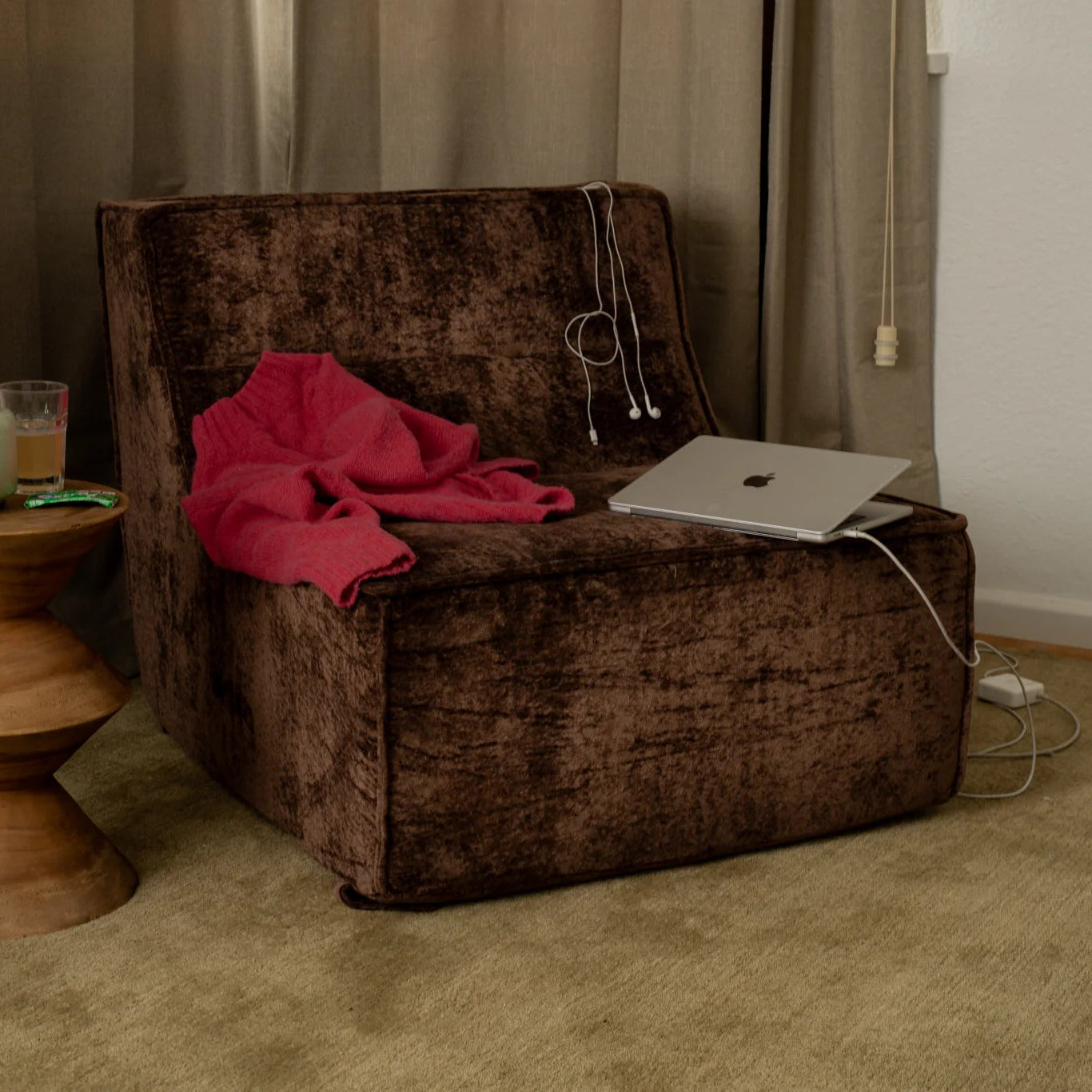 Brown armchair with a pink blanket and laptop, next to a wooden side table with a glass and candle.