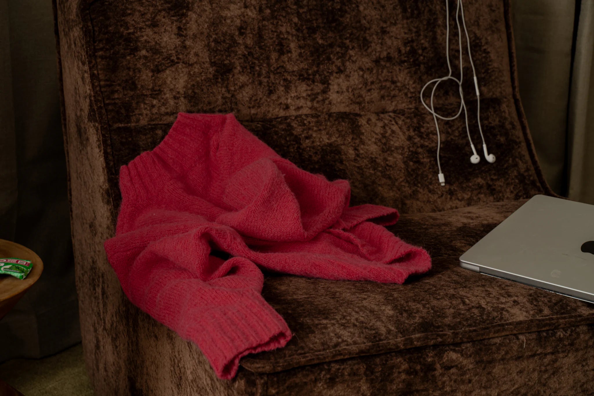 Red sweater on a brown textured chair with a laptop and earphones nearby.