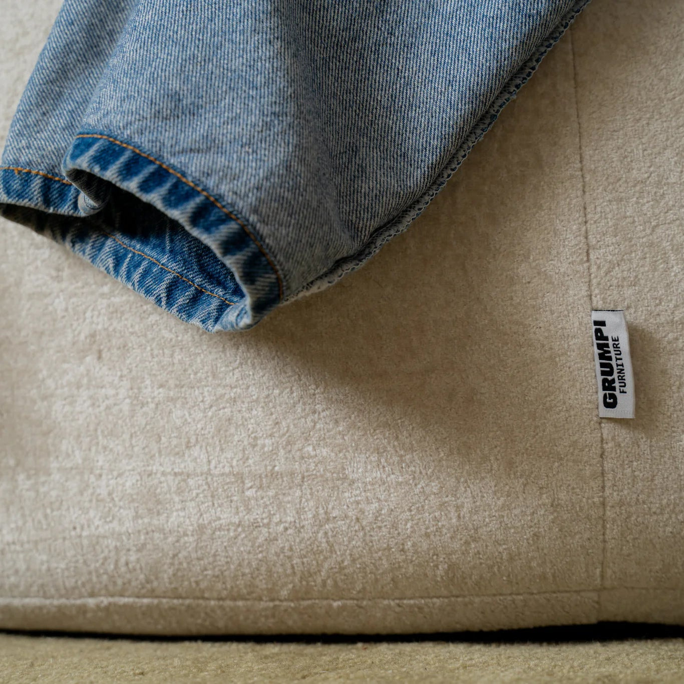 Close-up of a beige cushion with a denim edge and a visible 'Grumpi' label.