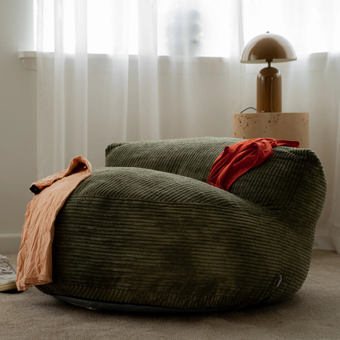Green bean bag chair with a red blanket in a room with white curtains and a lamp.