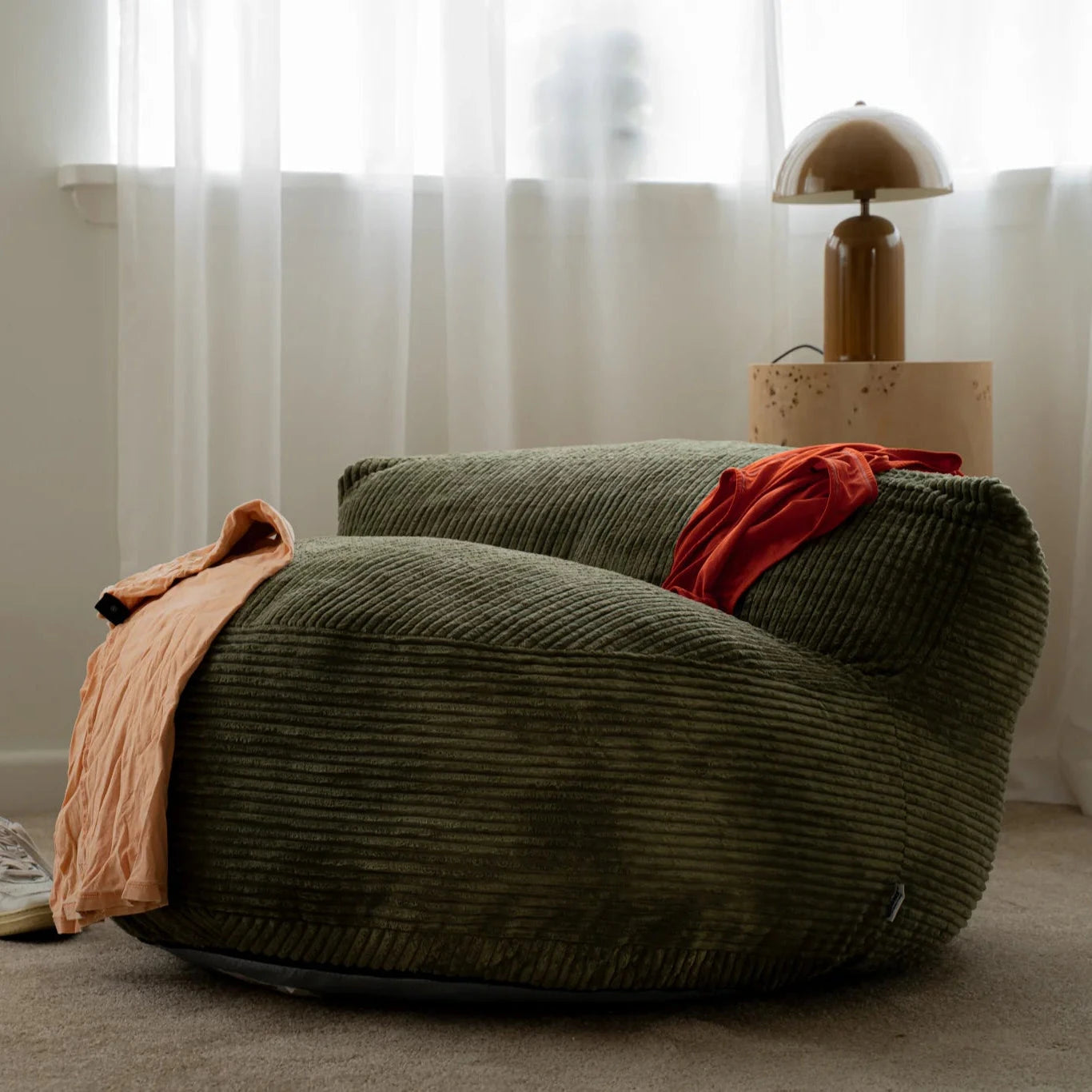 Green bean bag chair with a red blanket in a room with white curtains and a lamp.