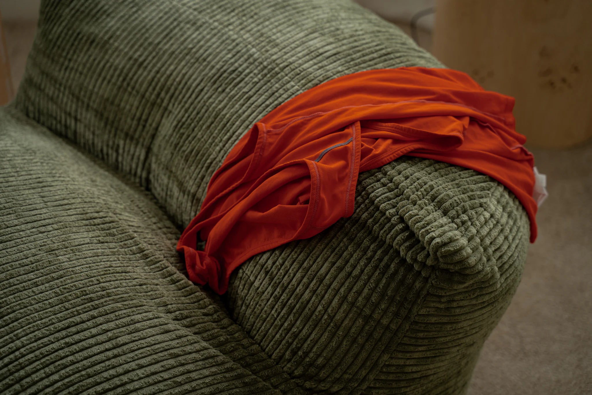 Green textured armchair with a red garment draped over it on a neutral background