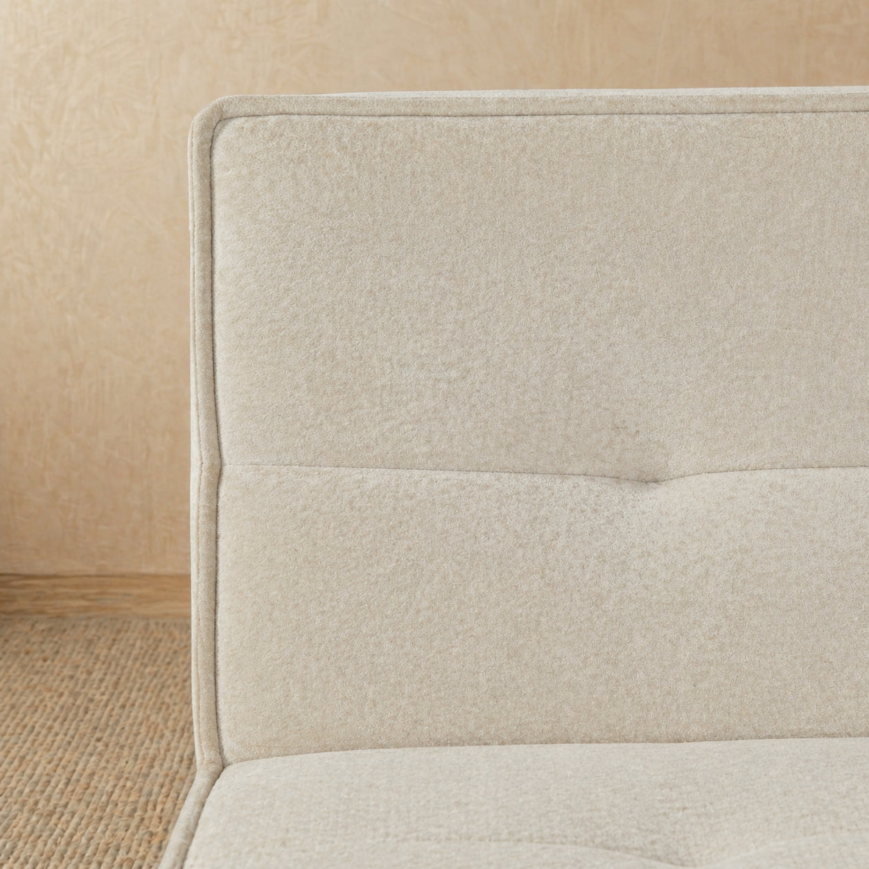 Close-up of a beige upholstered headboard on a bed with a wooden floor.