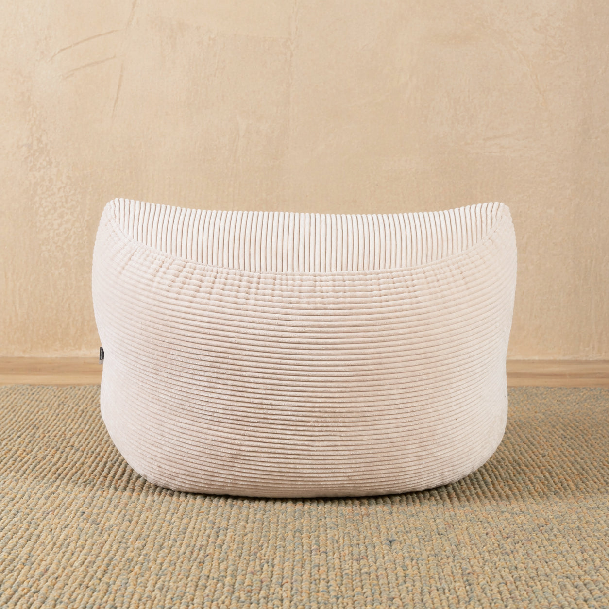 Beige textured ottoman on a beige carpet with a beige wall background