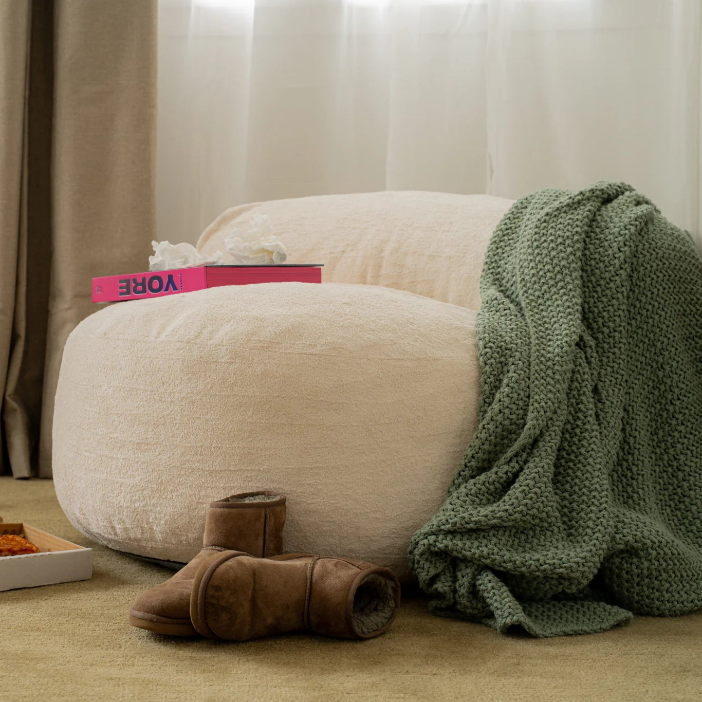 Beige armchair with a green blanket and small table in a room with curtains.