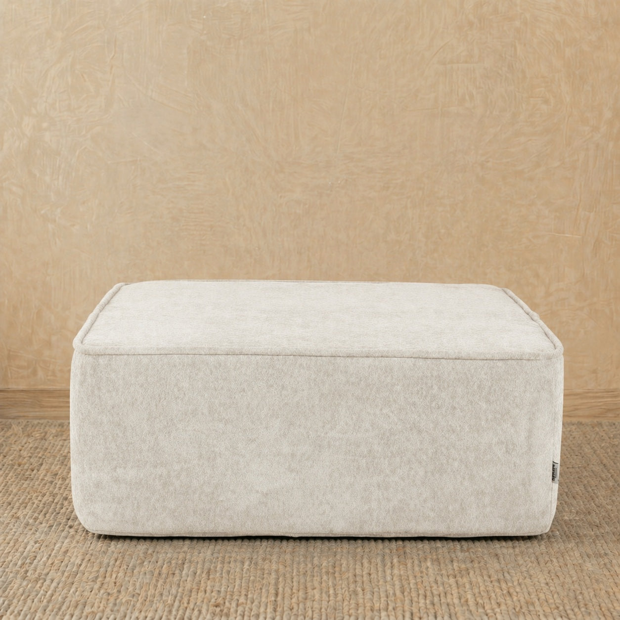 Beige ottoman on a wooden floor with a beige wall background