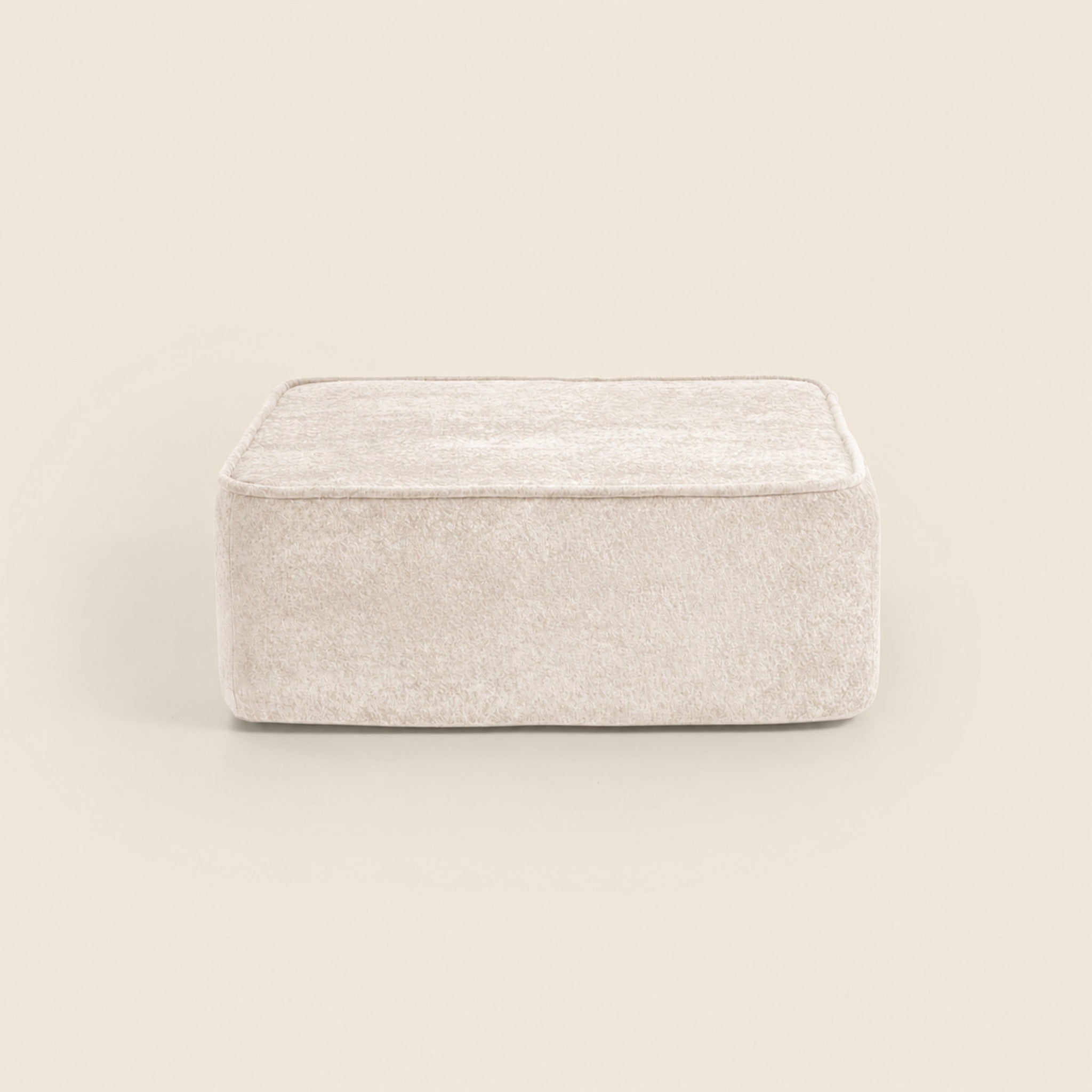 Cream textured square ottoman on a beige background.