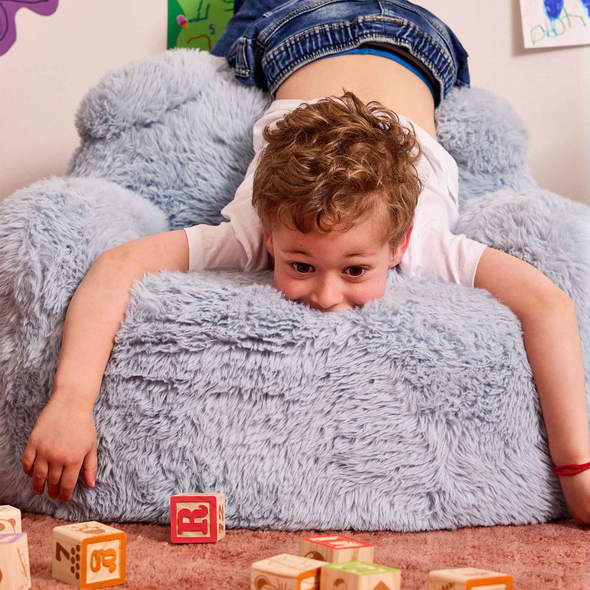 Grinning boy lying across the seat of the blue Beari Kids Armchair