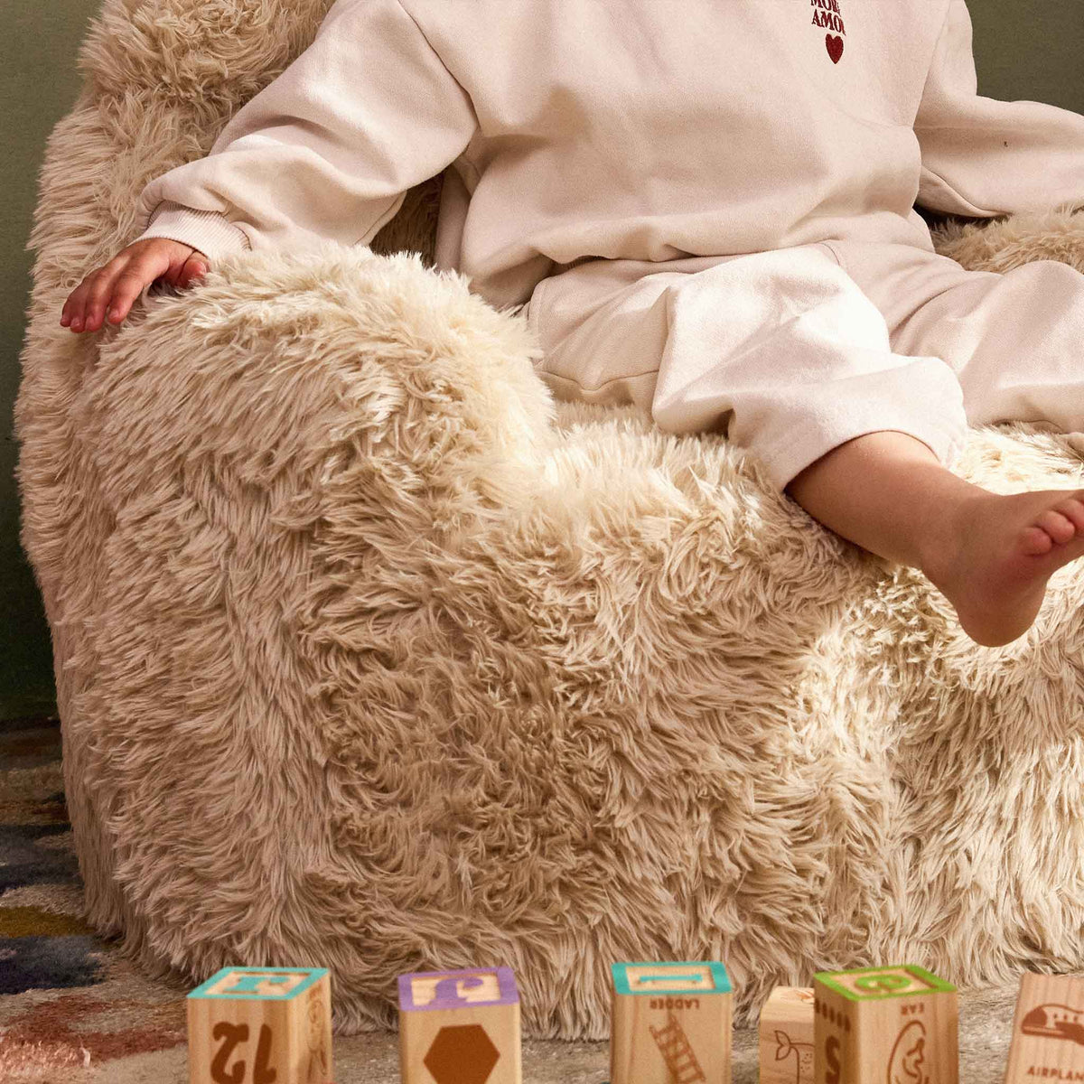 Close-up of a child sitting on the cream faux fur seat of the Beari Kids Armchair