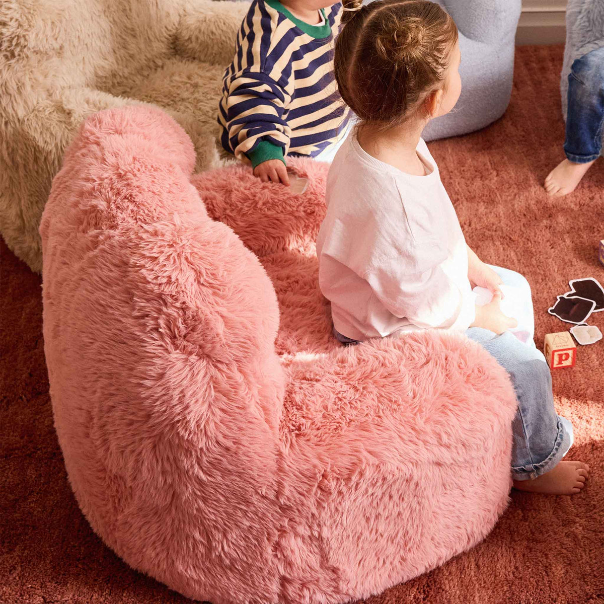 Toddler sitting in the pink Beari Kids Armchair with other children nearby