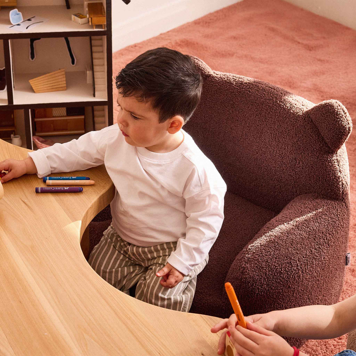 Boy sitting in the brown Teddi Kids Armchair drawing with crayons at a low wooden table