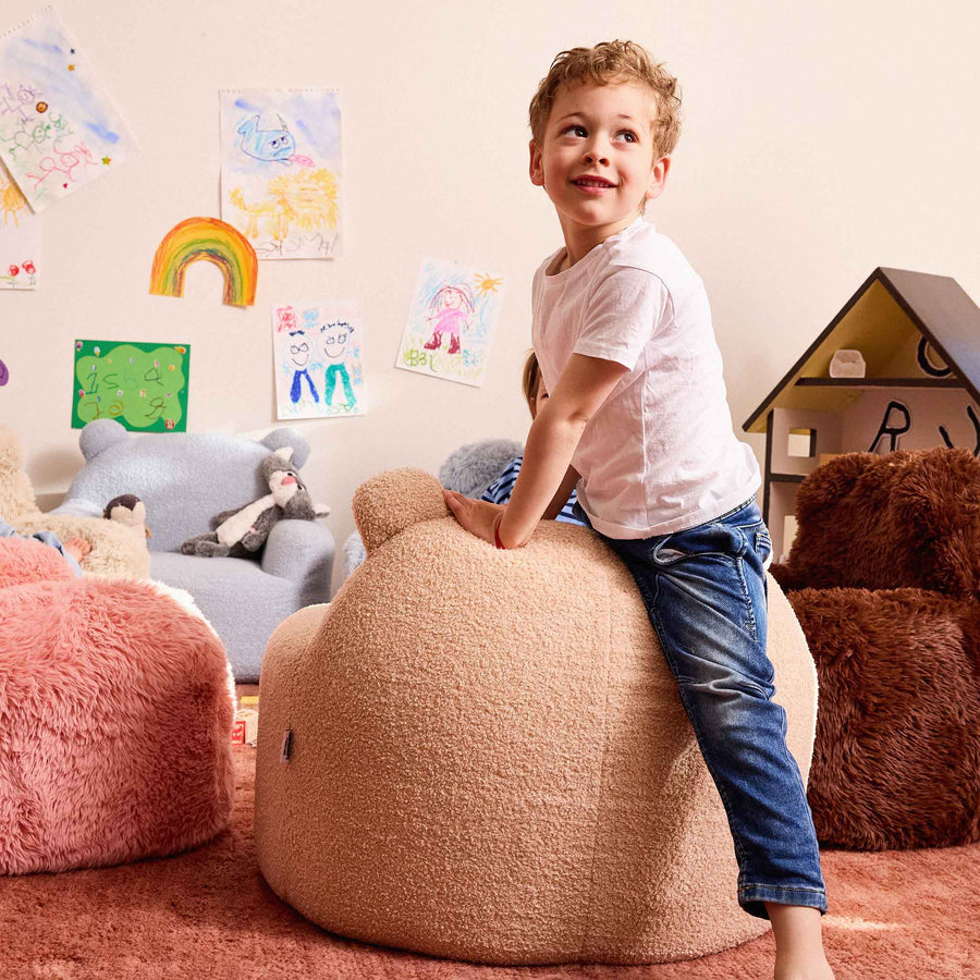 Boy climbing on the cream Teddi Kids Armchair in a playroom with drawings on the wall #color_cream-teddy