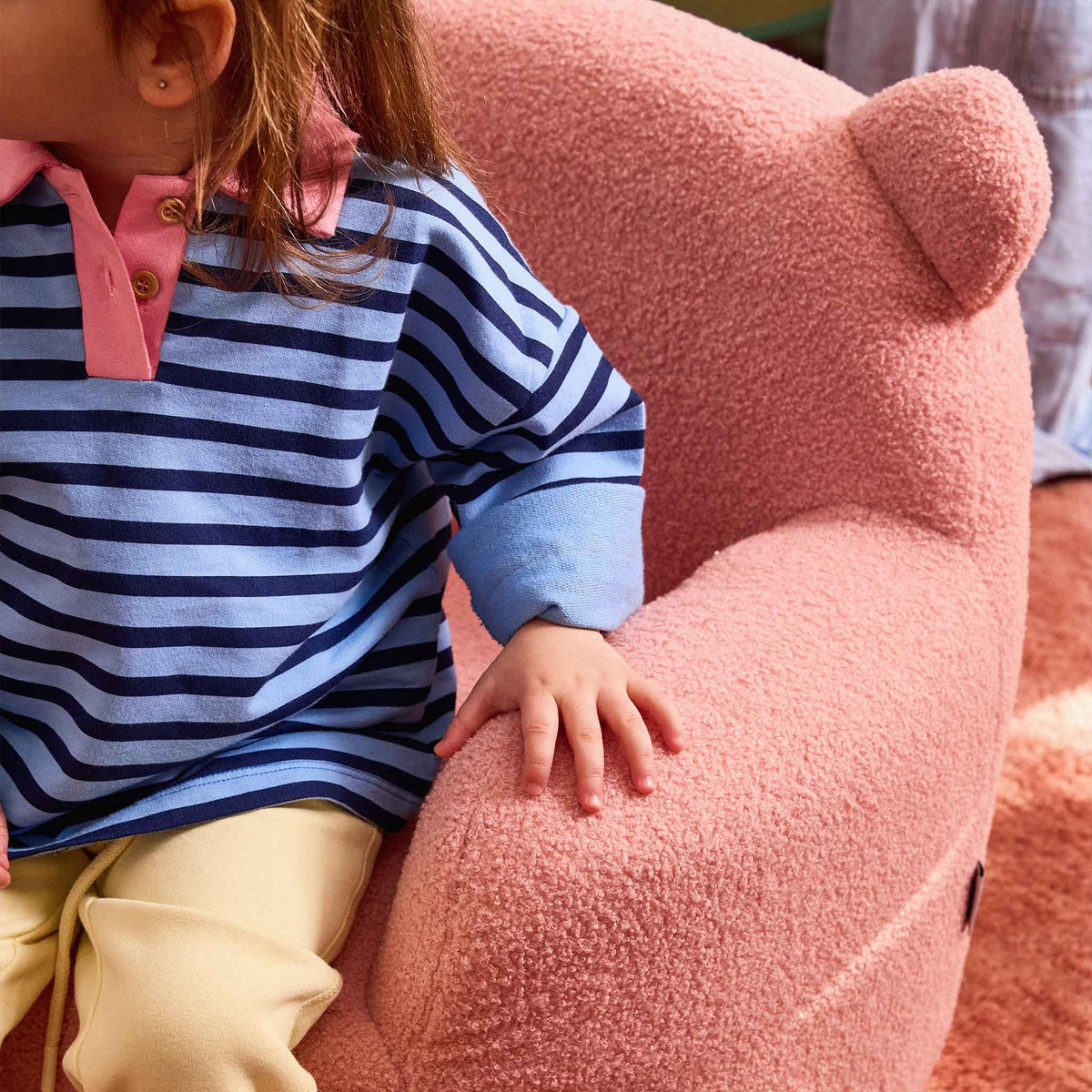 Child resting a hand on the arm of the pink Teddi Kids Armchair