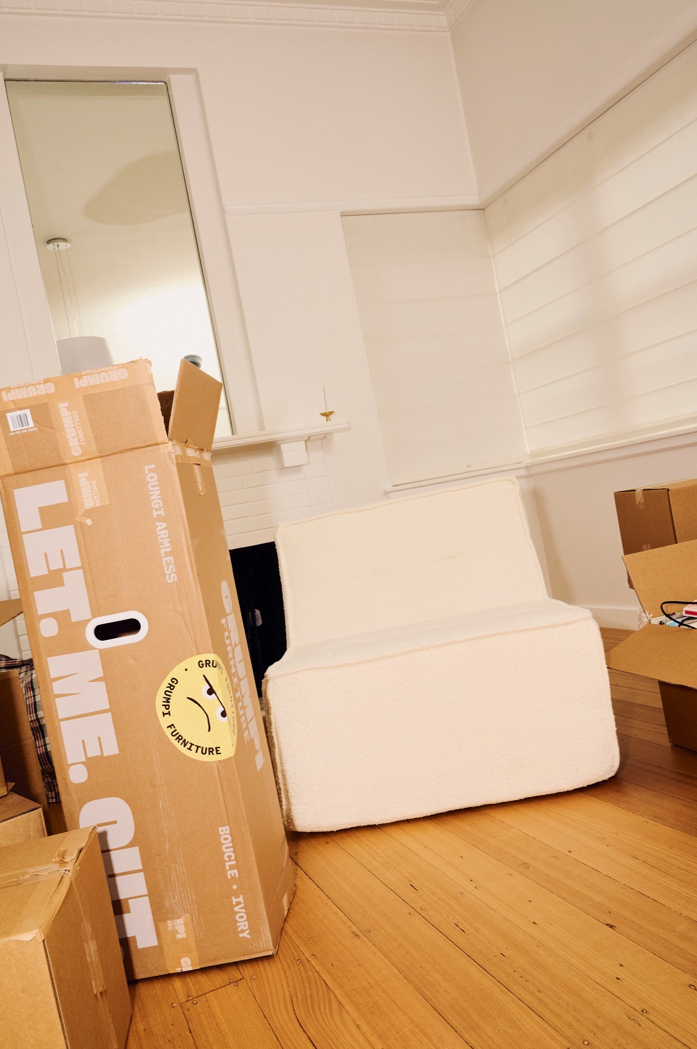 Unpacked cardboard box labeled 'Let Me Curl' on a wooden floor with a white couch in the background. 