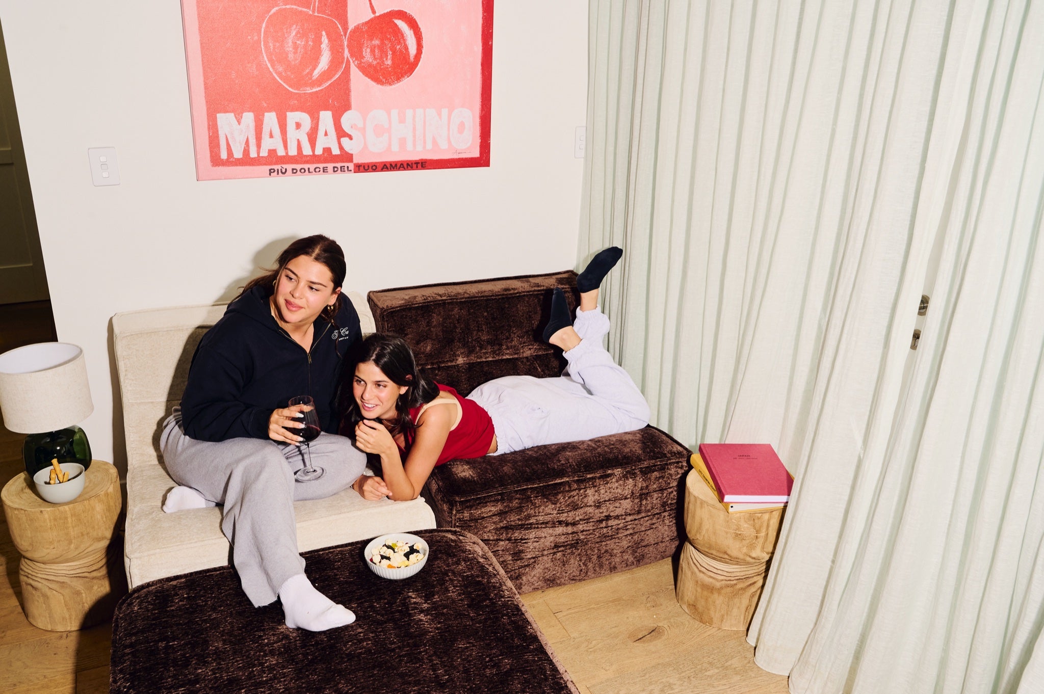 Two people sitting on a couch with a 'Maraschino' poster in the background 
