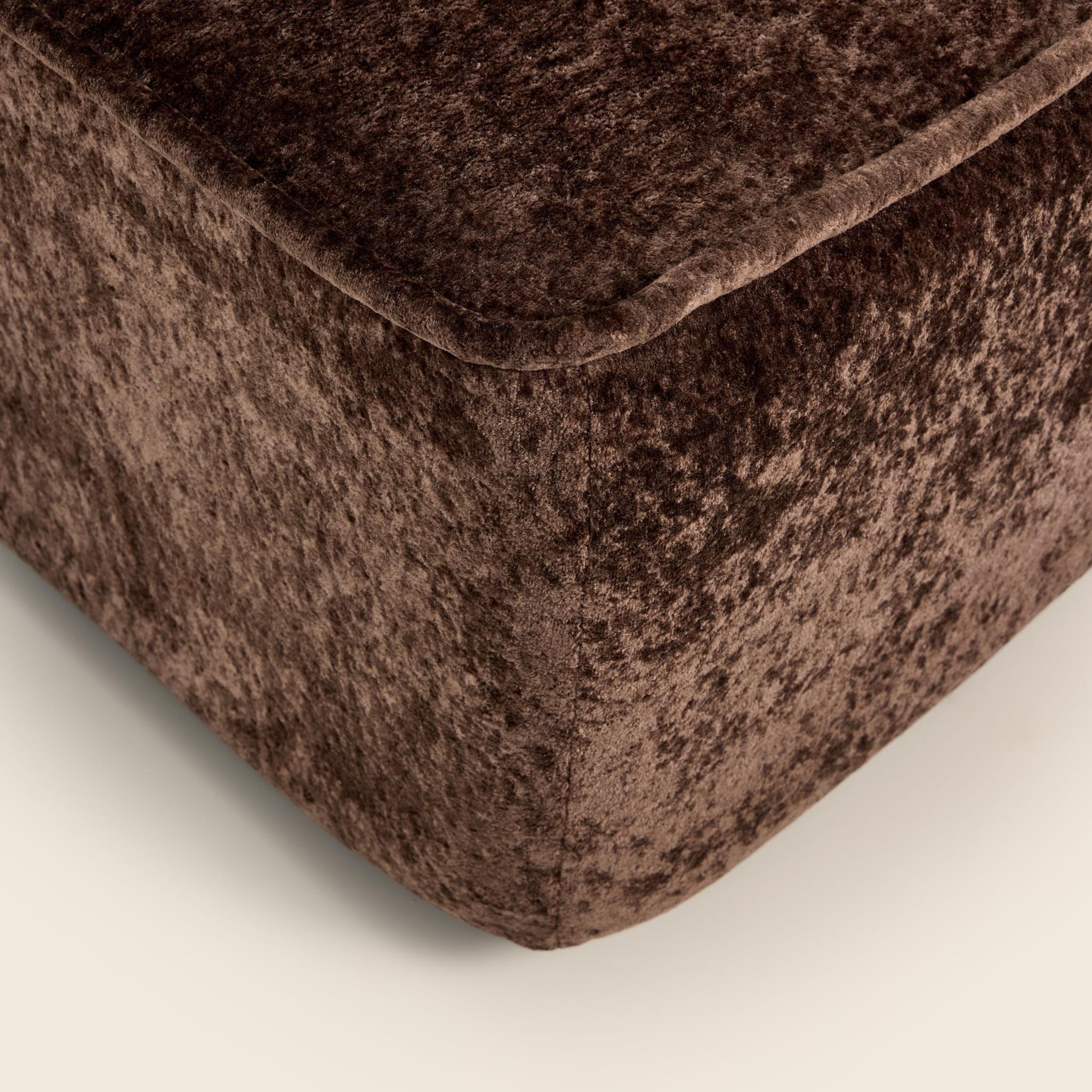 Close-up of a brown textured ottoman corner on a light beige background

