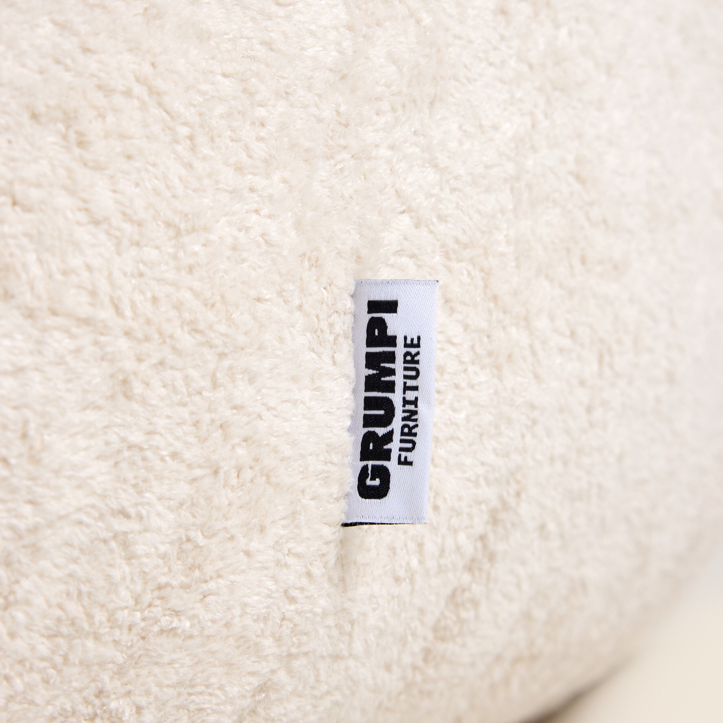 Close-up of a textured beige fabric with a 'GRUMPI FURNITURE' label.
