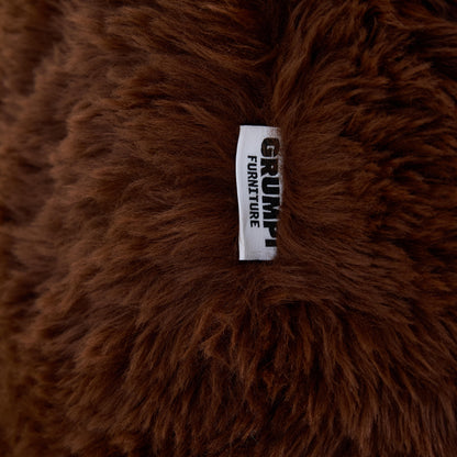 Close-up of a brown fluffy pillow with a 'Grumpi Furniture' label.

