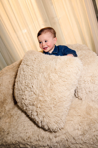 Child sitting inside a large fluffy chair with curtains in the background 