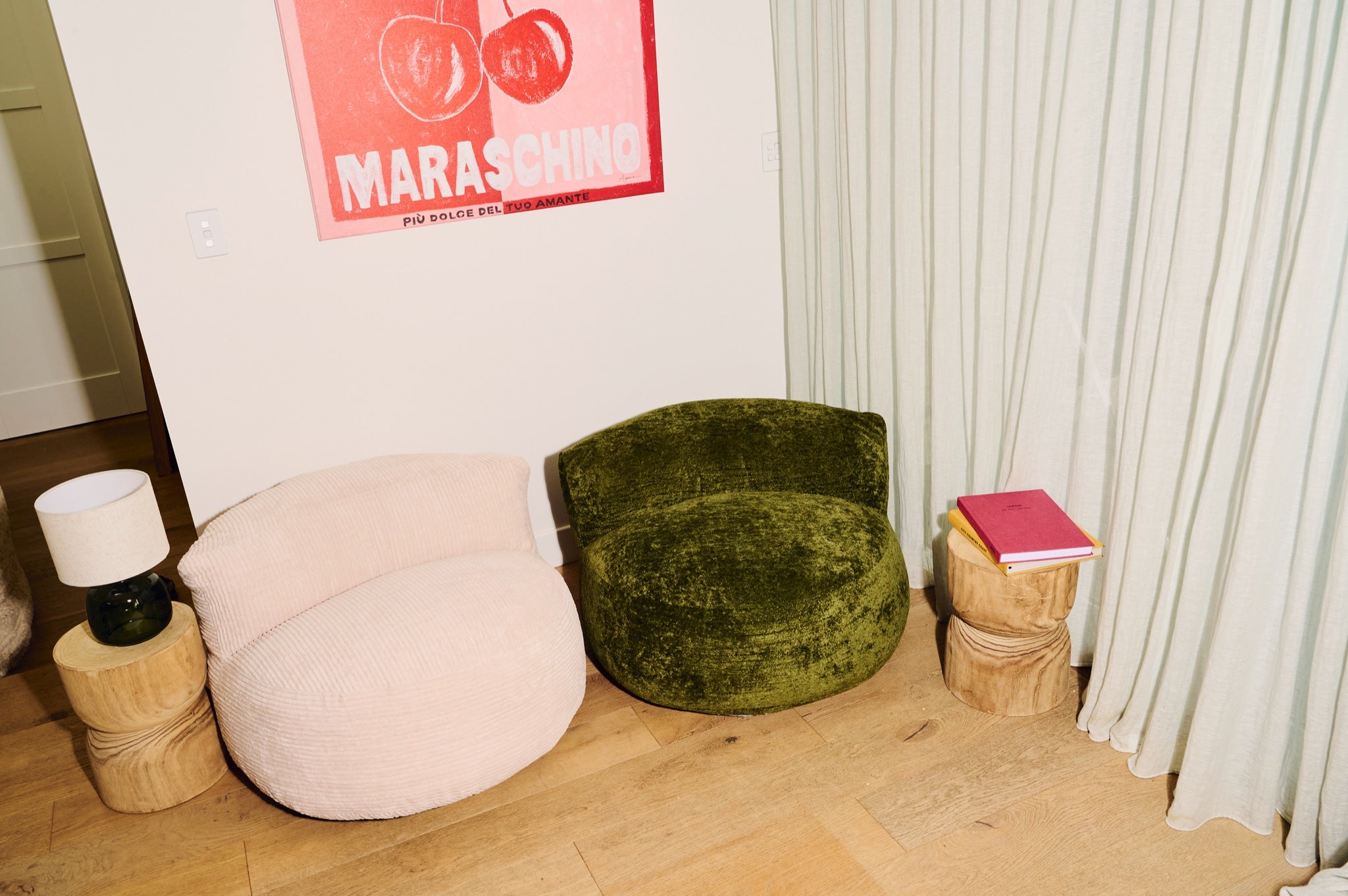 Green velvet chair and pink bean bag against a white wall with a red poster. 