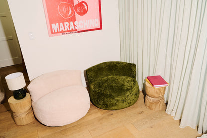 Green velvet chair and pink bean bag against a white wall with a red poster. 
