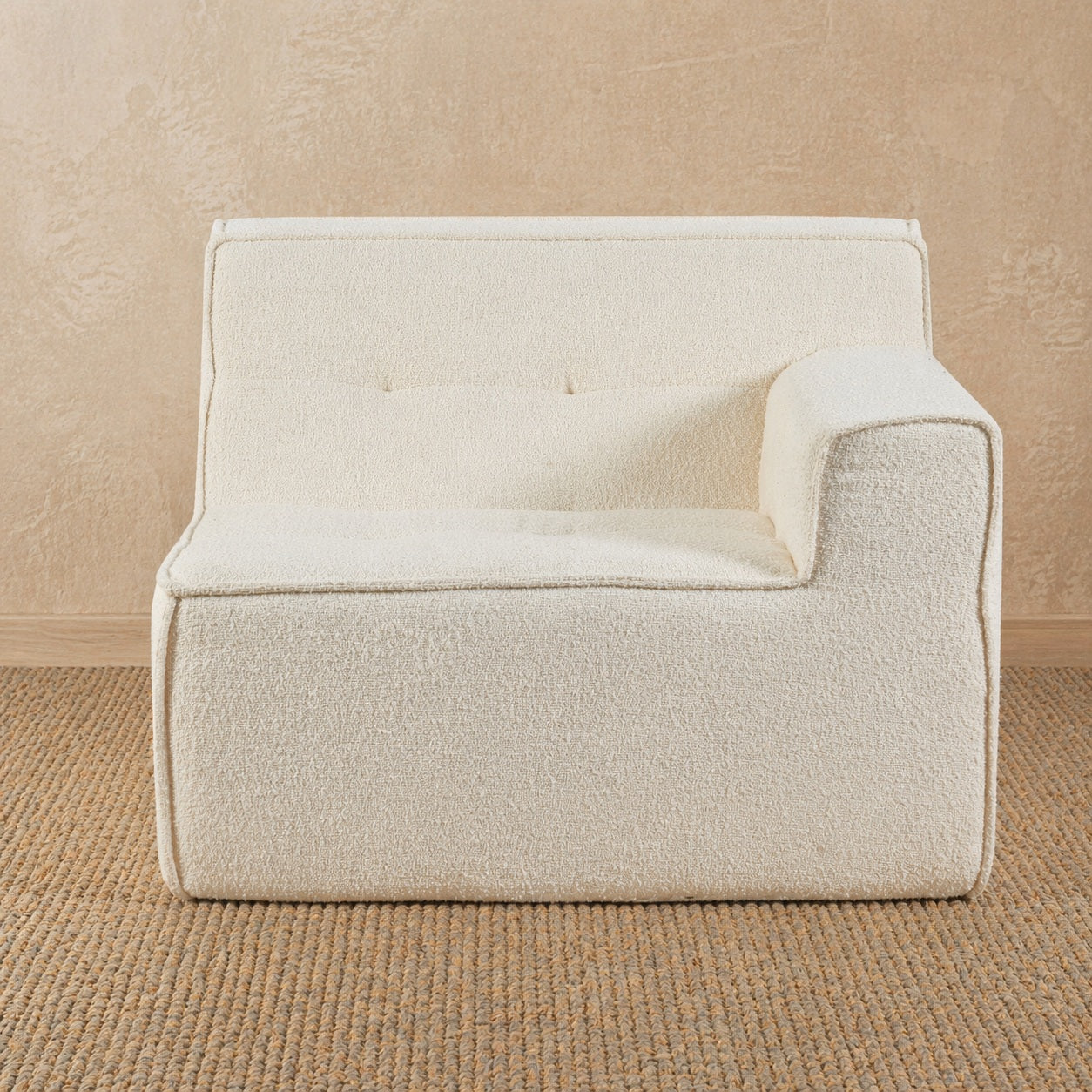 Beige armchair against a beige wall on a textured brown floor 