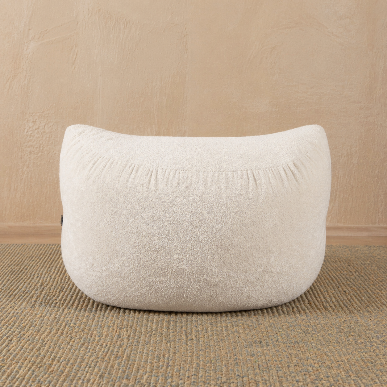 White textured cushion on a beige carpet with a beige wall background 