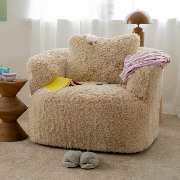 Beige fluffy armchair in a room with a small wooden table and slippers on the floor.