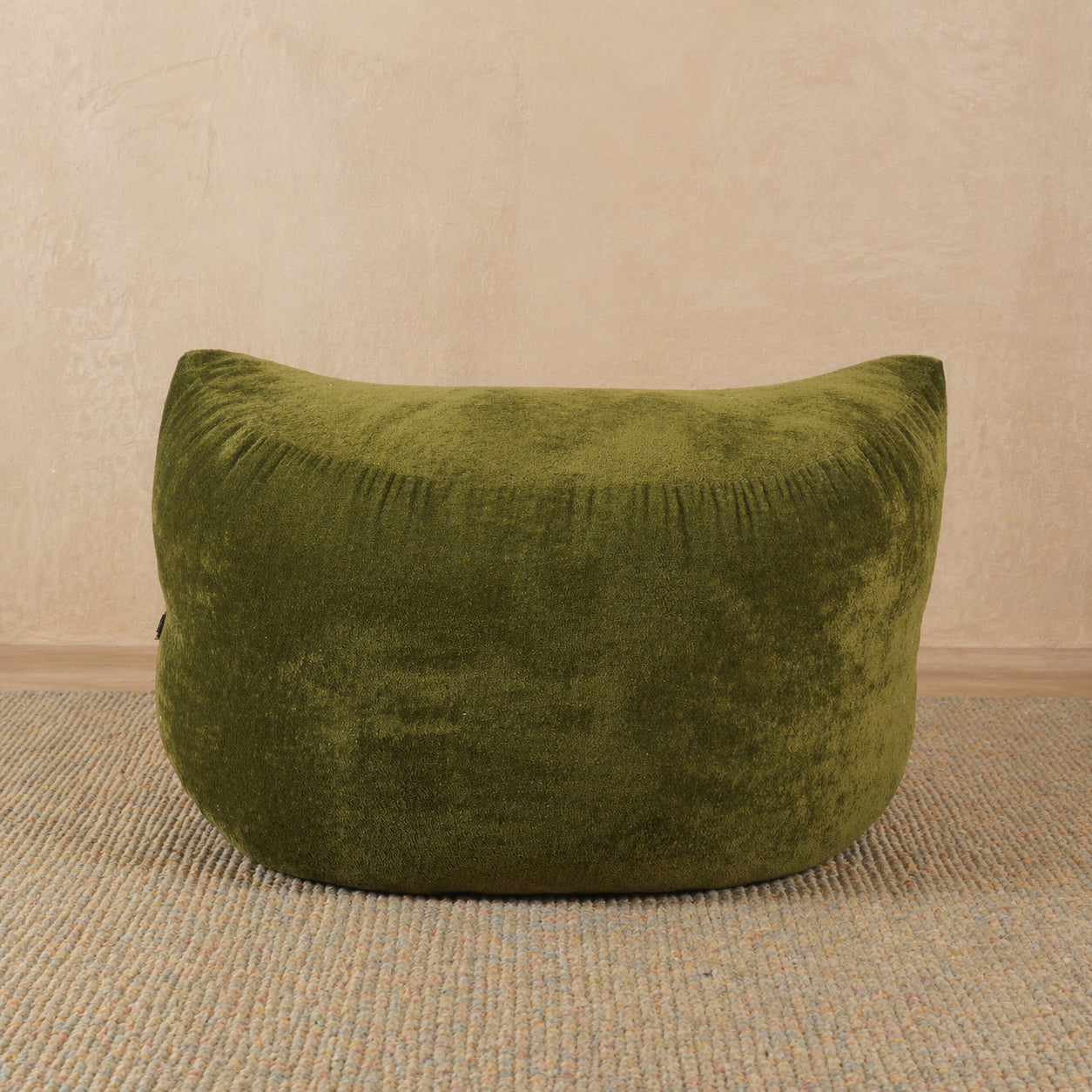 Green bean bag chair on a beige carpet with a beige wall background 