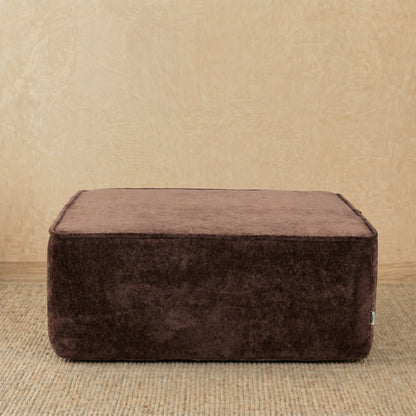 Brown ottoman on a beige carpet with a beige wall background 