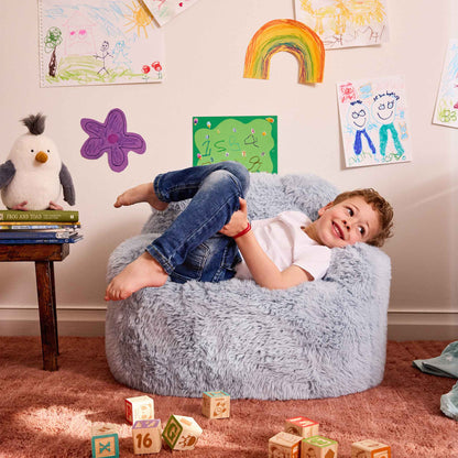 Boy lounging with his legs over the arm of the blue Beari Kids Armchair 