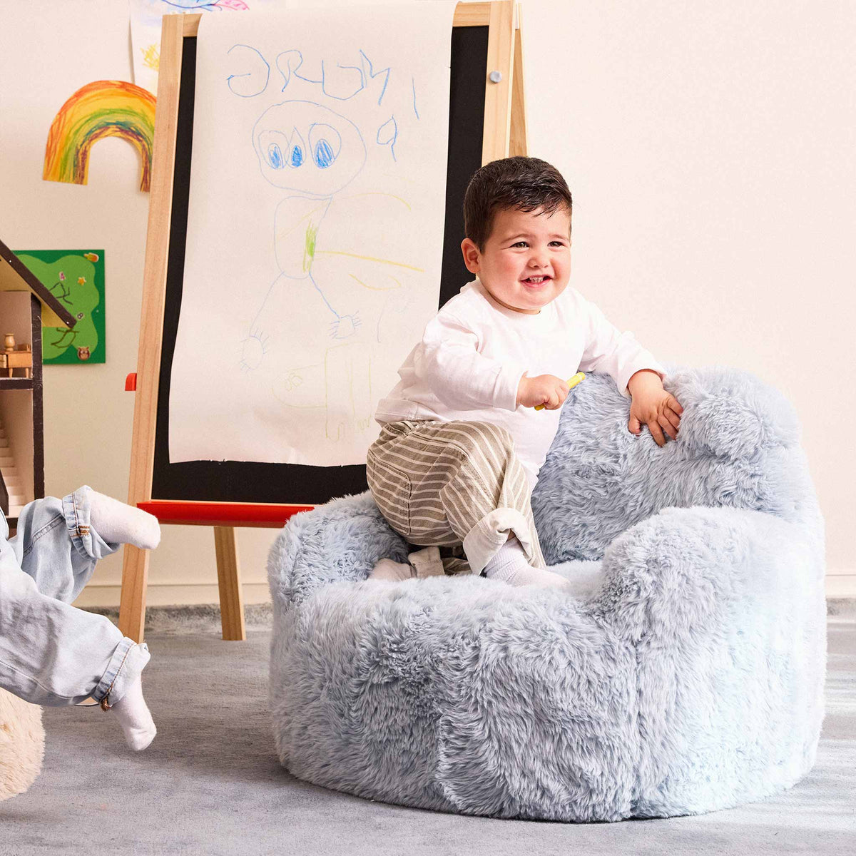Toddler climbing into the blue Beari Kids Armchair beside an easel 