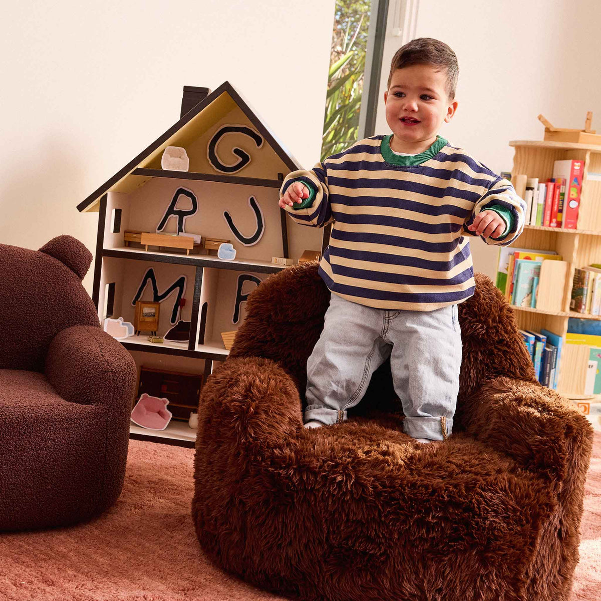 Toddler standing up in the brown Beari Kids Armchair in front of a dollhouse 