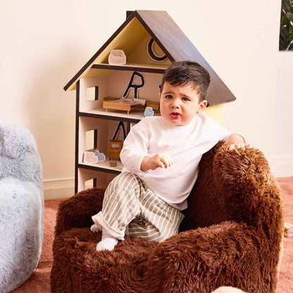 Toddler sitting in the brown Beari Kids Armchair beside a wooden dollhouse 