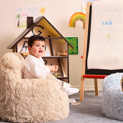 Toddler sitting in the cream Beari Kids Armchair beside a dollhouse and easel 