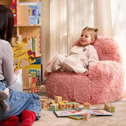 Girl relaxing in the pink Beari Kids Armchair while a grown-up reads a picture book 