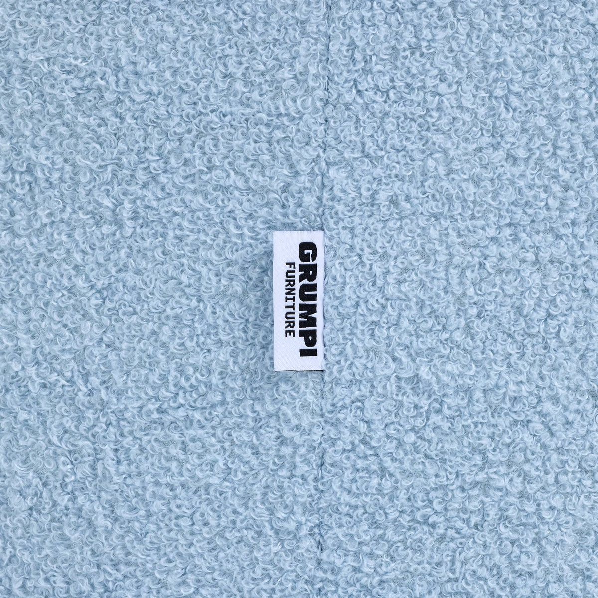 Close-up of the blue teddy fabric on the Teddi Kids Armchair, with the Grumpi Furniture label 