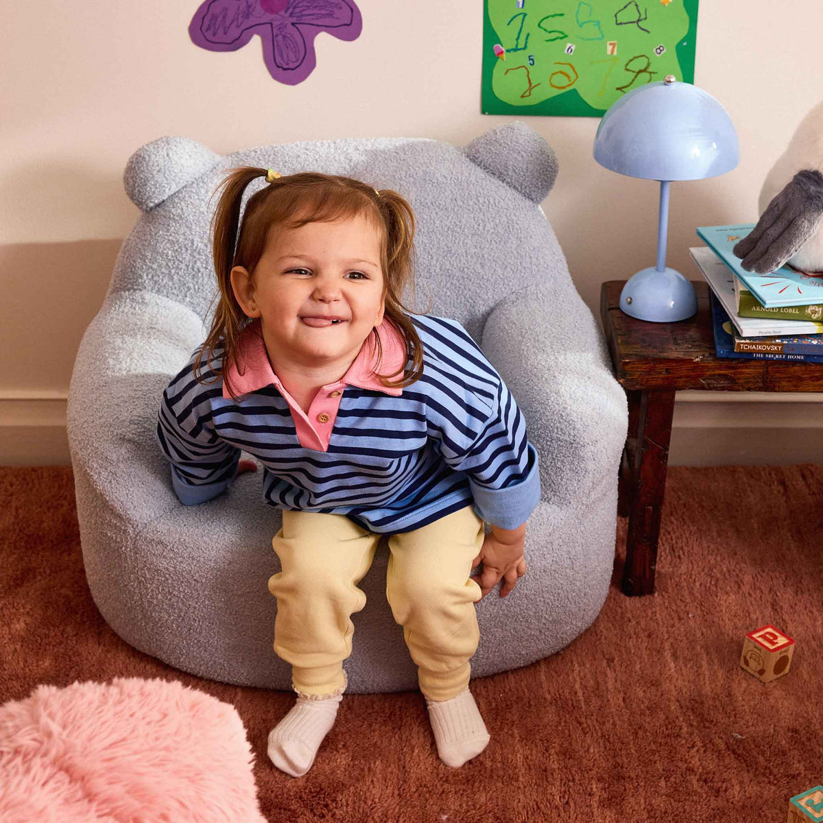 Smiling girl in a striped jumper sitting in the blue Teddi Kids Armchair 