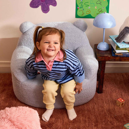 Smiling girl in a striped jumper sitting in the blue Teddi Kids Armchair 