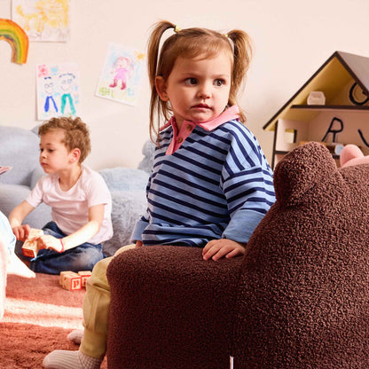 Little girl sitting in the brown Teddi Kids Armchair in a playroom 