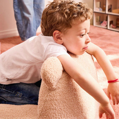 Toddler leaning over the back of the cream Teddi Kids Armchair 