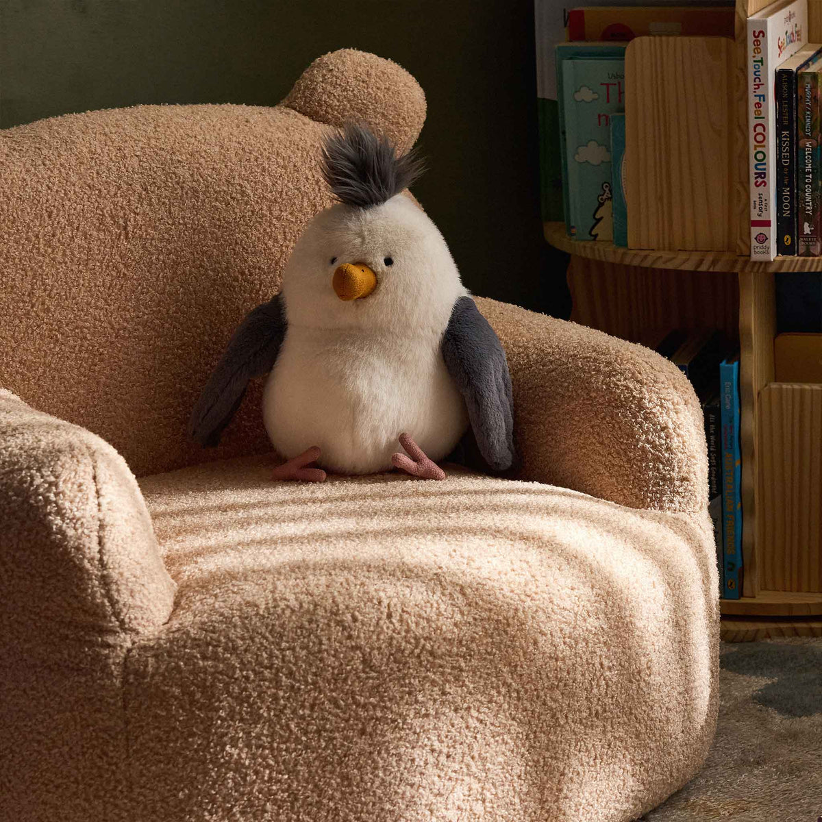 Cream Teddi Kids Armchair with a plush toy on the seat, beside a bookshelf 