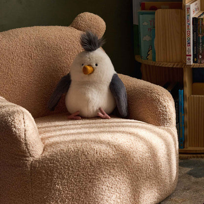 Cream Teddi Kids Armchair with a plush toy on the seat, beside a bookshelf 