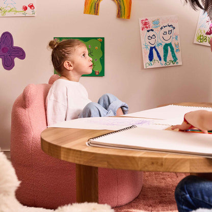 Girl sitting in the pink Teddi Kids Armchair at a low wooden table with a sketchbook 