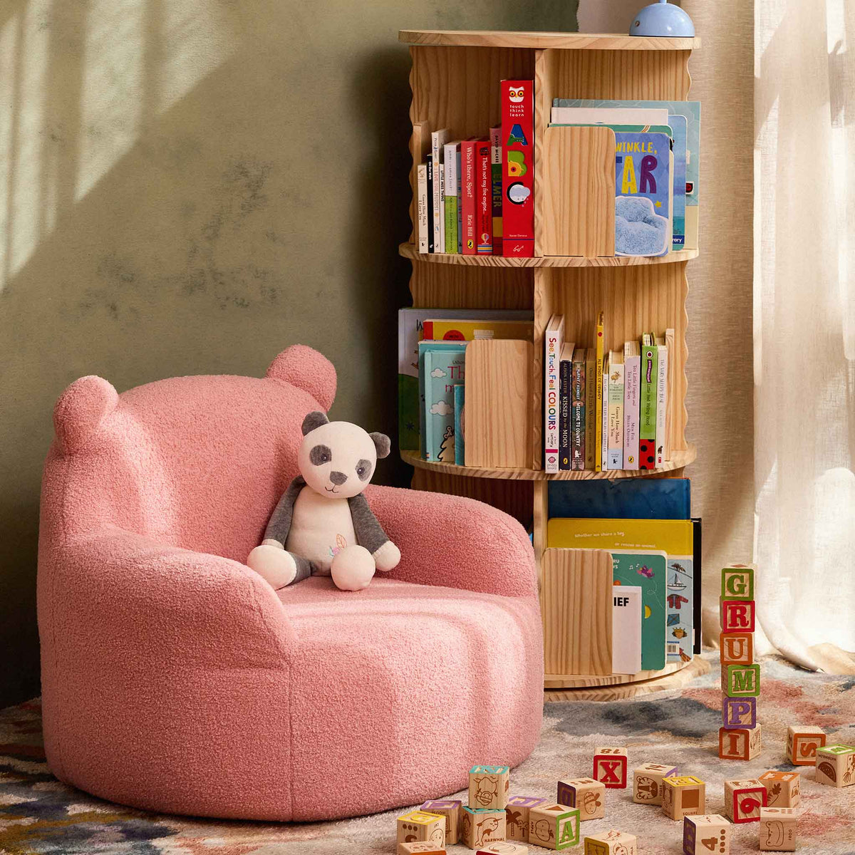 Pink Teddi Kids Armchair with a plush panda in a reading nook beside a bookshelf 